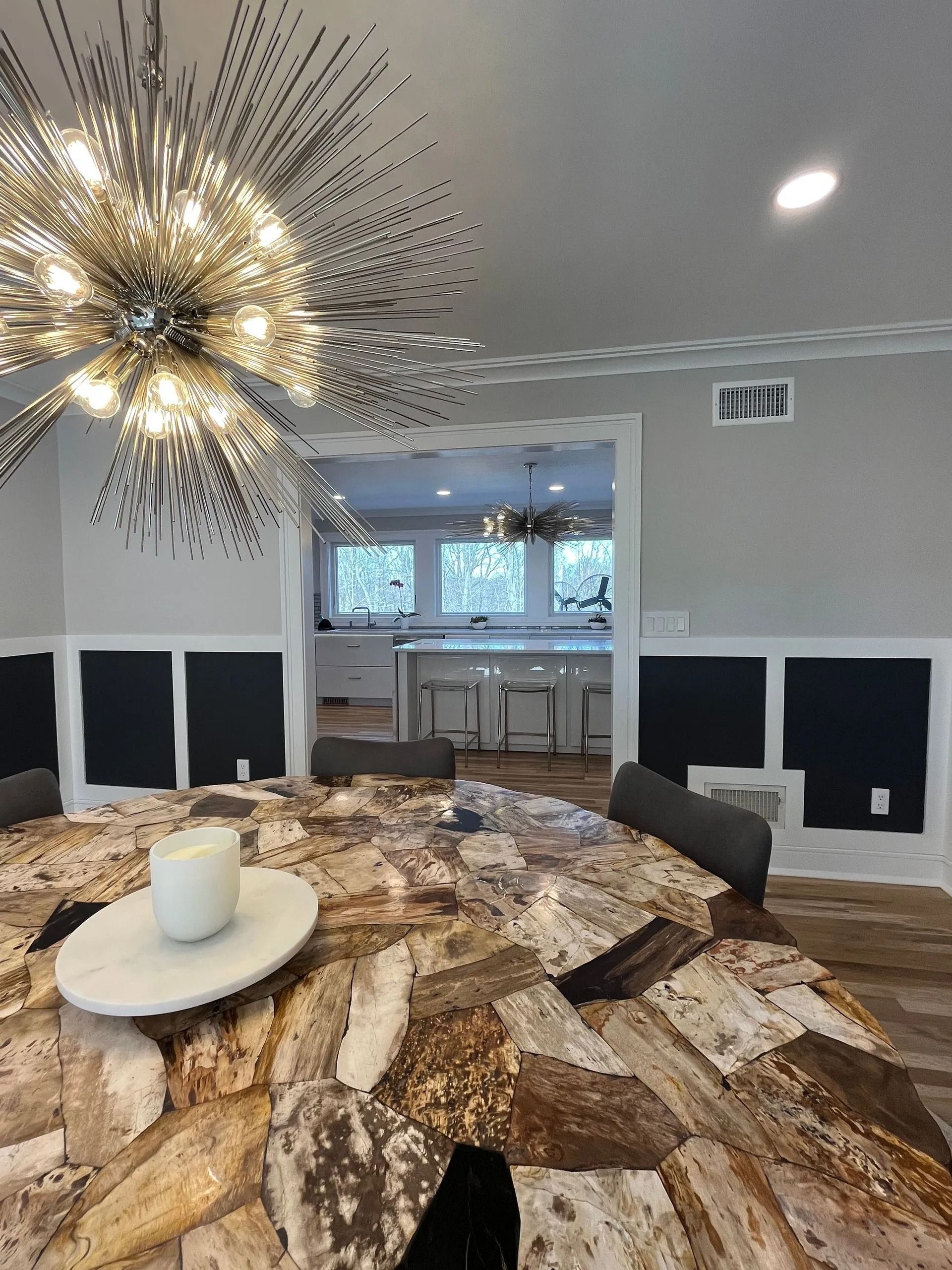 Dining room with large patterned table, black paneling, and a view into a kitchen.