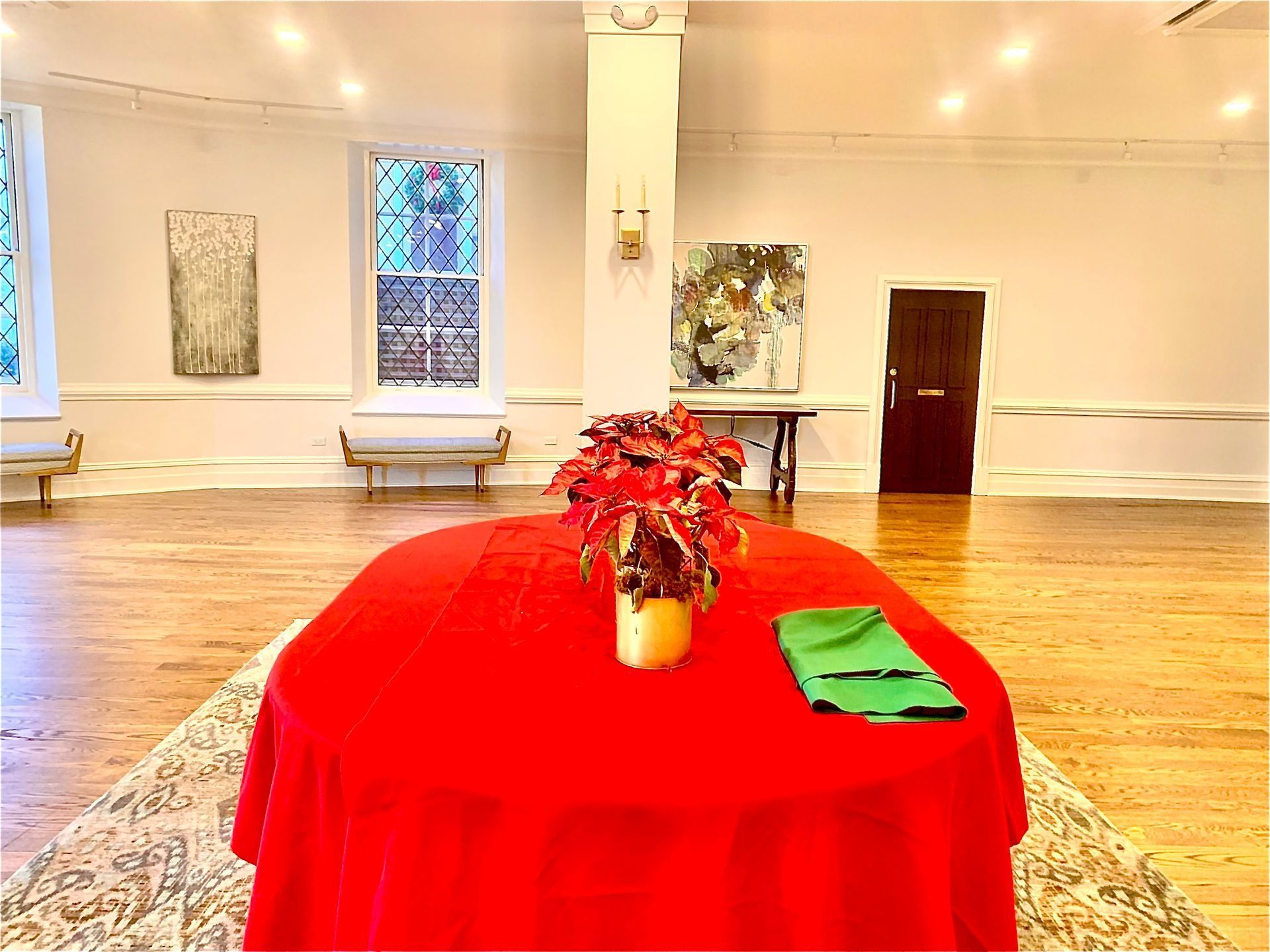 A large, red tablecloth on a rug in a bright room, with a vase of red flowers on it.