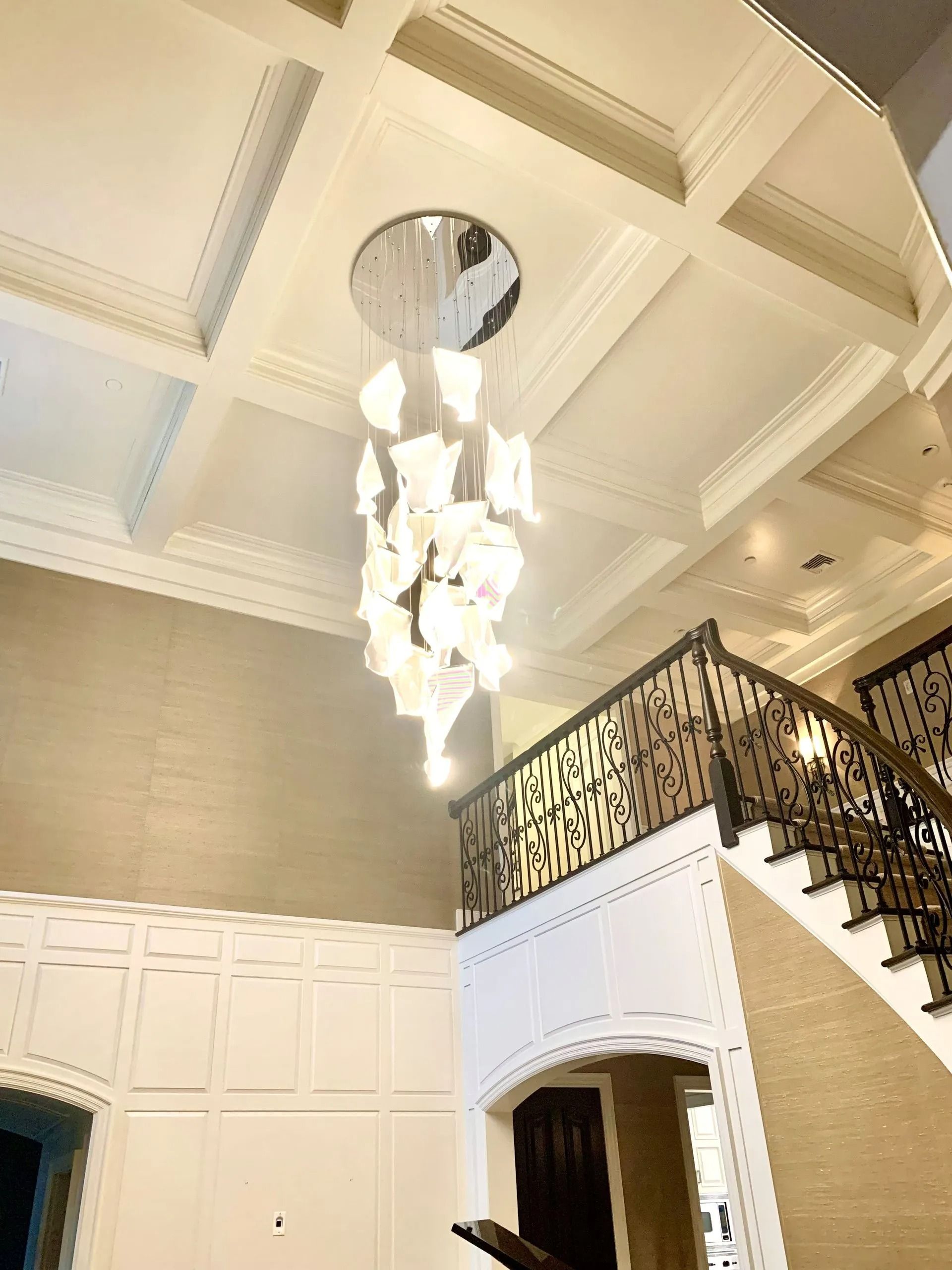 Elegant foyer with a coffered ceiling and ornate chandelier near a staircase.