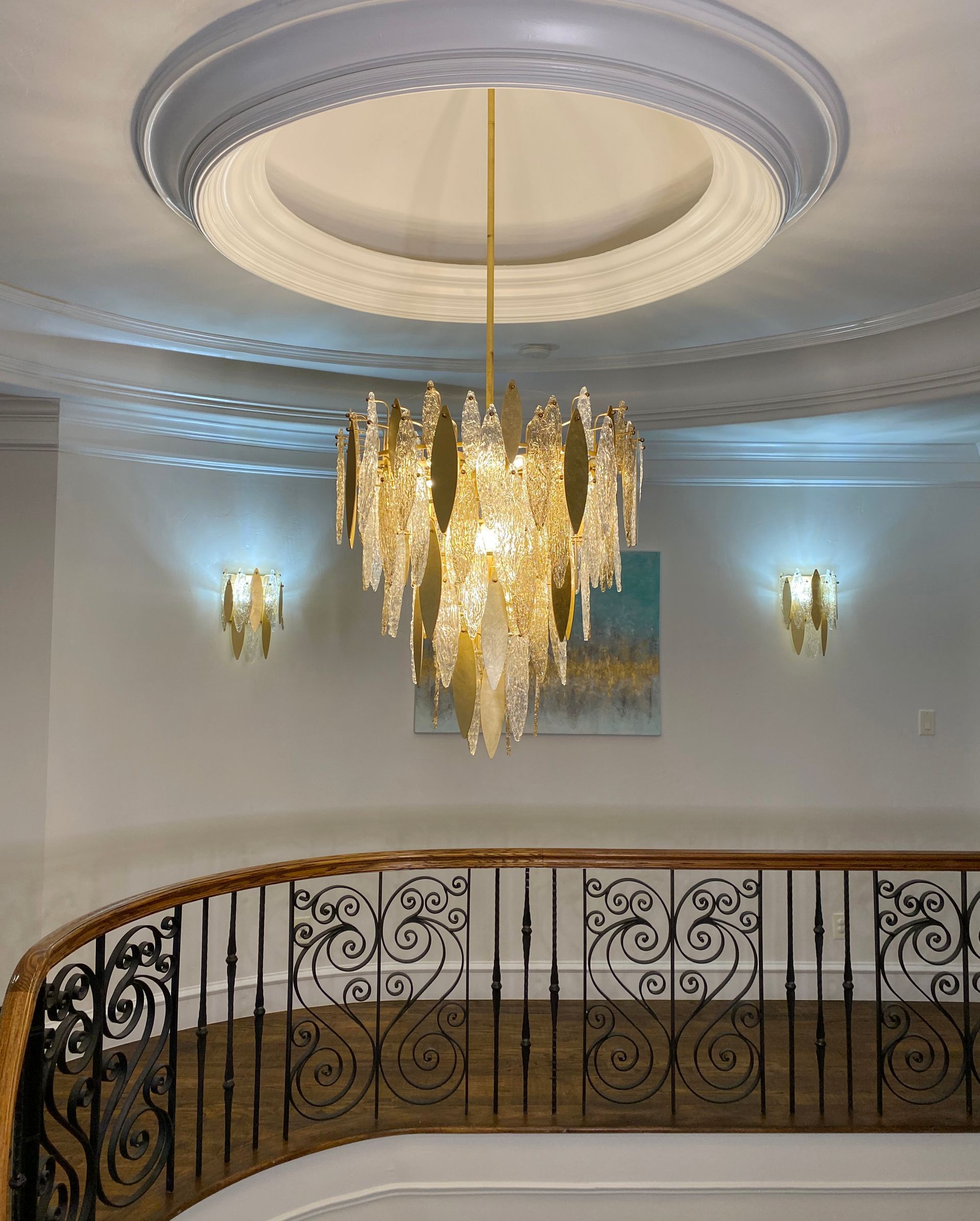 Elegant foyer with gold chandelier, ornate railing, and white ceiling moldings