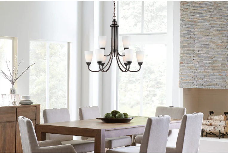Bright dining room with a wooden table, upholstered chairs, chandelier, and large windows on white walls