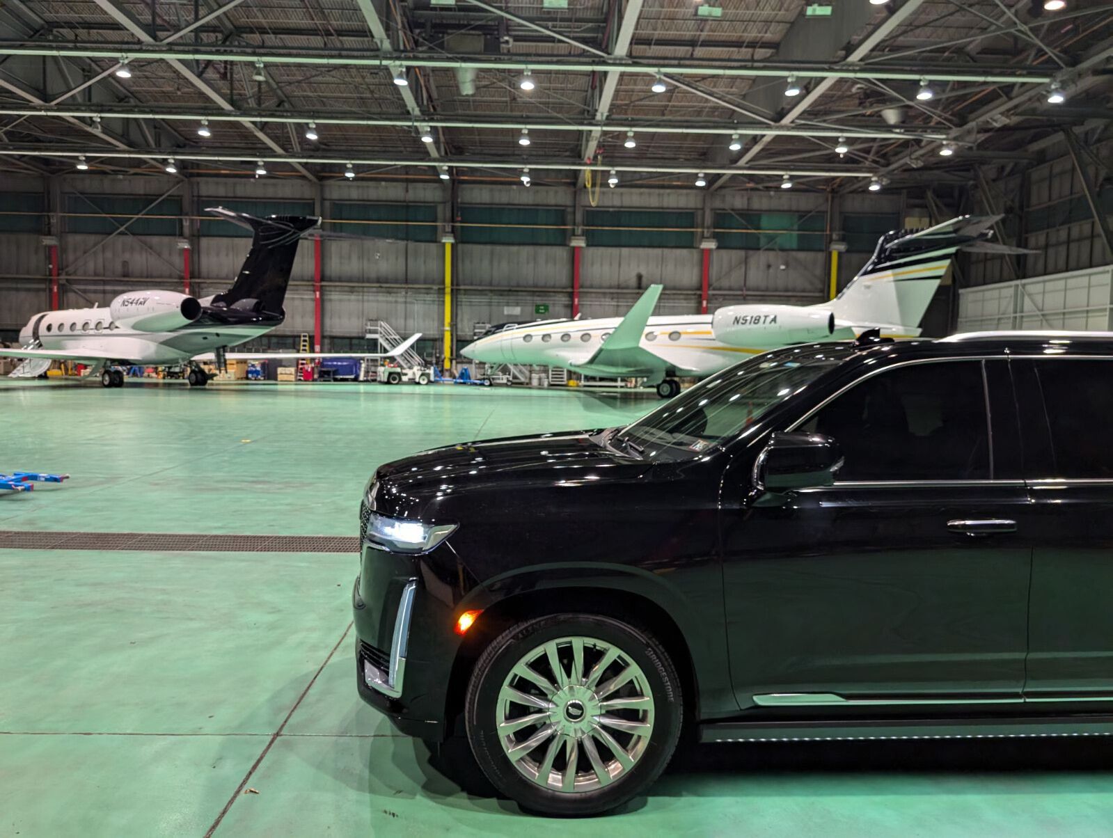 A black limo is parked in a hangar with planes parked in the background