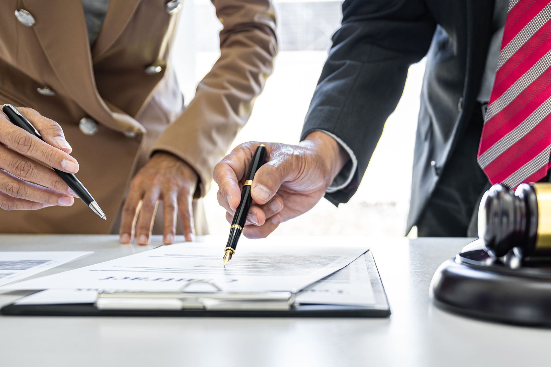 Two people reviewing documents, one pointing with a pen. Gavel on table.