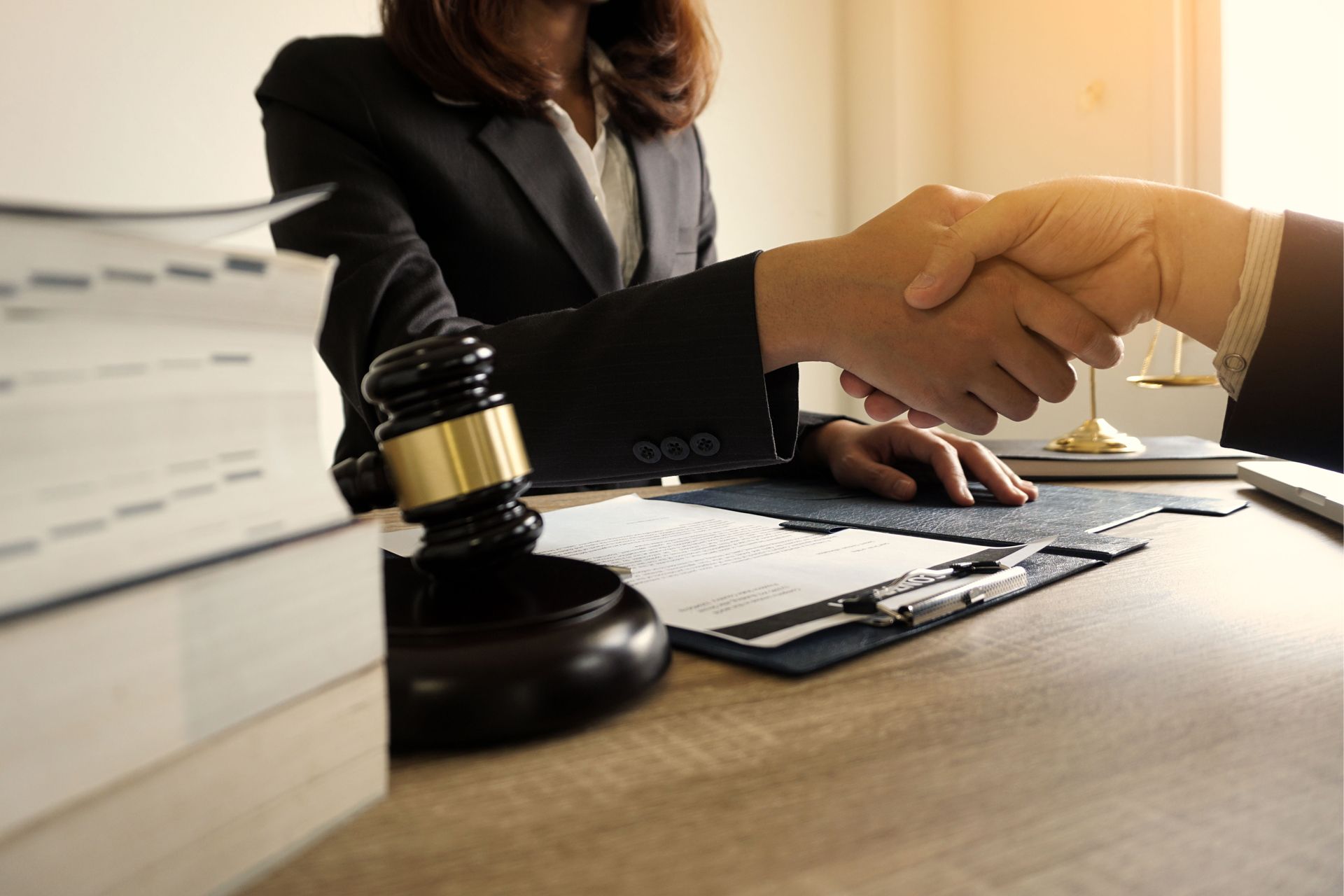 Two people shaking hands over a desk with a gavel and law books.