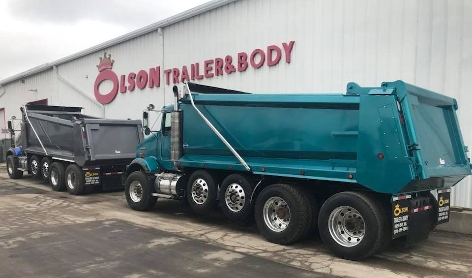 Two dump trucks are parked in front of a building that says olson trailer & body