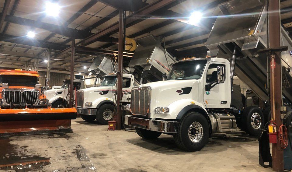A row of dump trucks are parked in a garage.