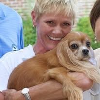 Woman holding a Cavalier King Charles Spaniel, both smiling, outdoors.