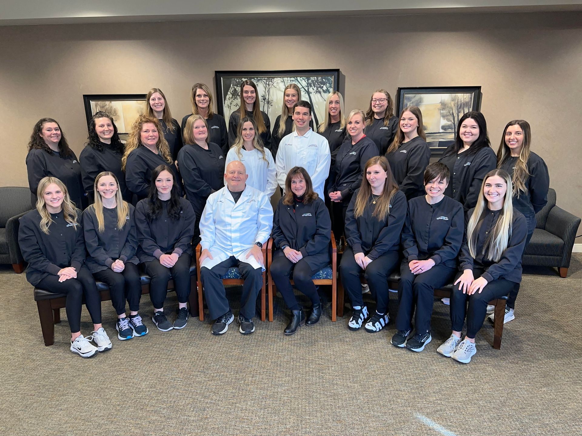 Group of people in black uniforms posing for a photo, seated and standing indoors.