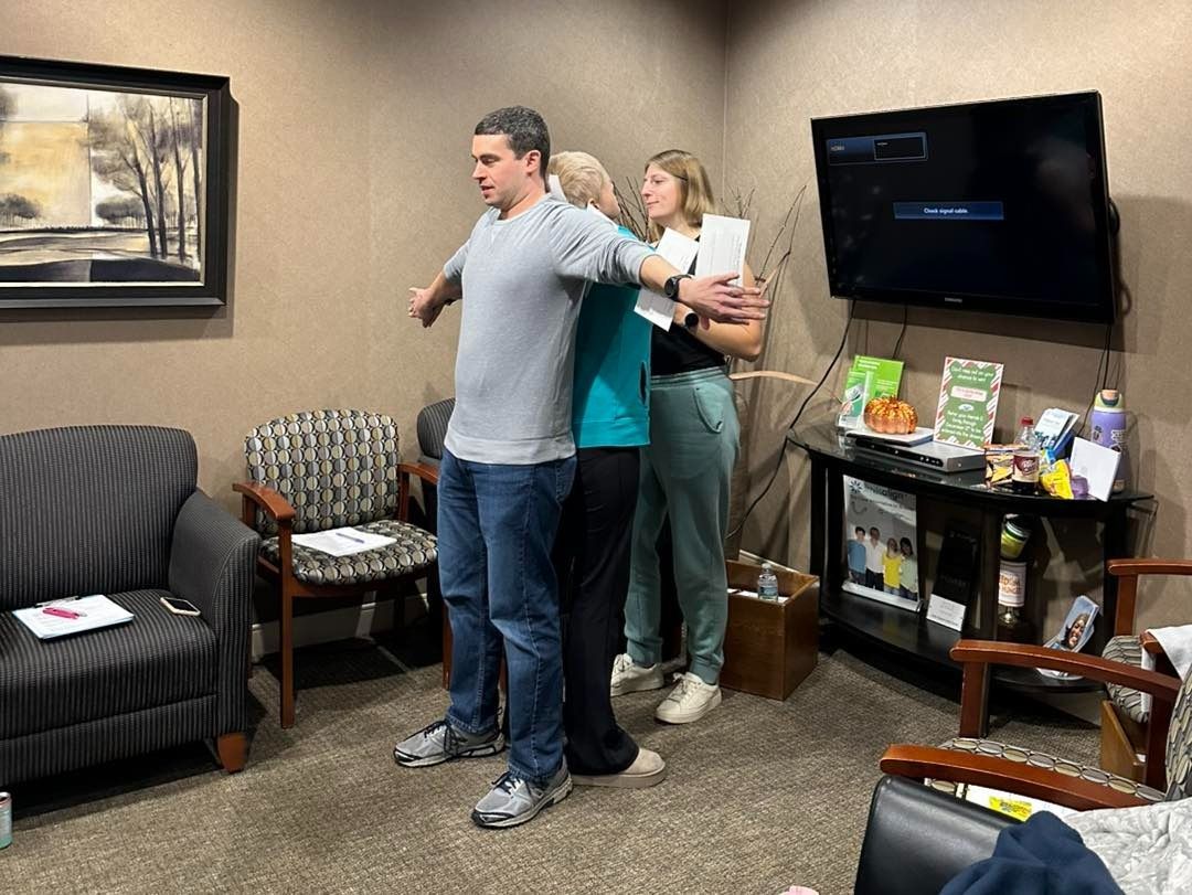 Three people stand close together in an office, arms around each other.