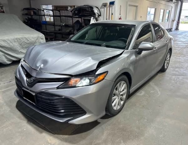 A silver car with a damaged hood is parked in a garage.