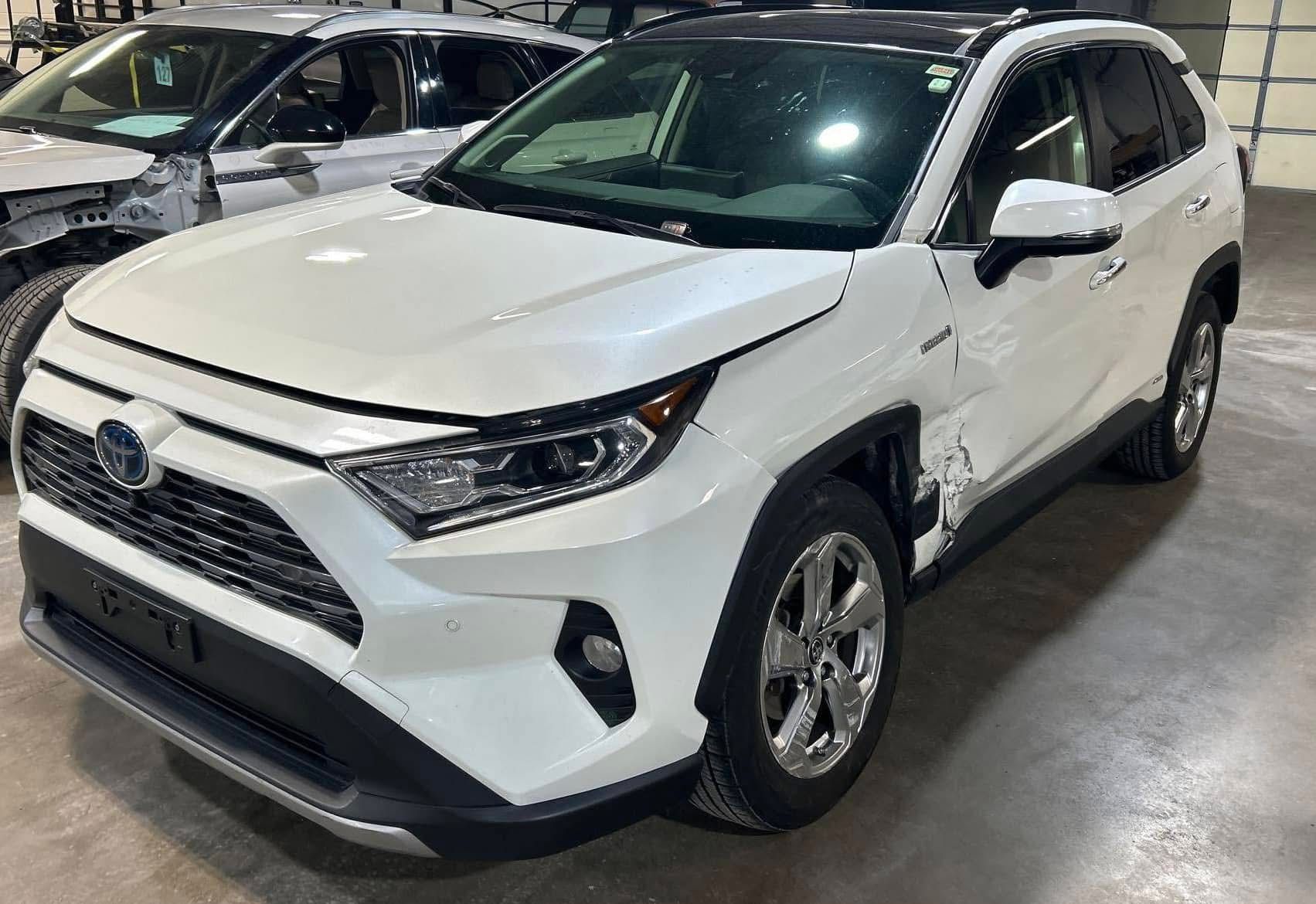 A white toyota rav4 is parked in a garage next to other cars.