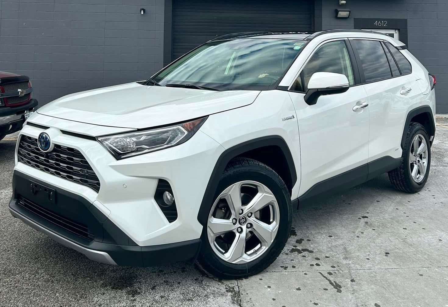 A white toyota rav4 hybrid is parked in front of a garage.
