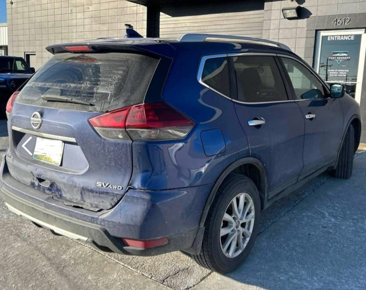 A blue nissan rogue is parked in front of a building.
