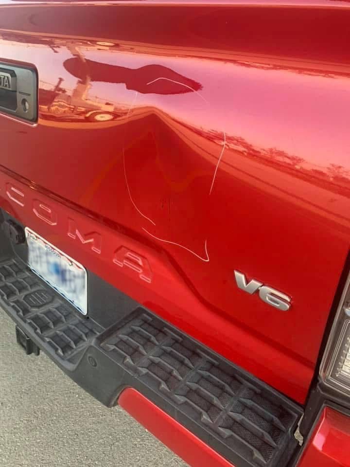 A red truck with a damaged tailgate is parked on the side of the road.