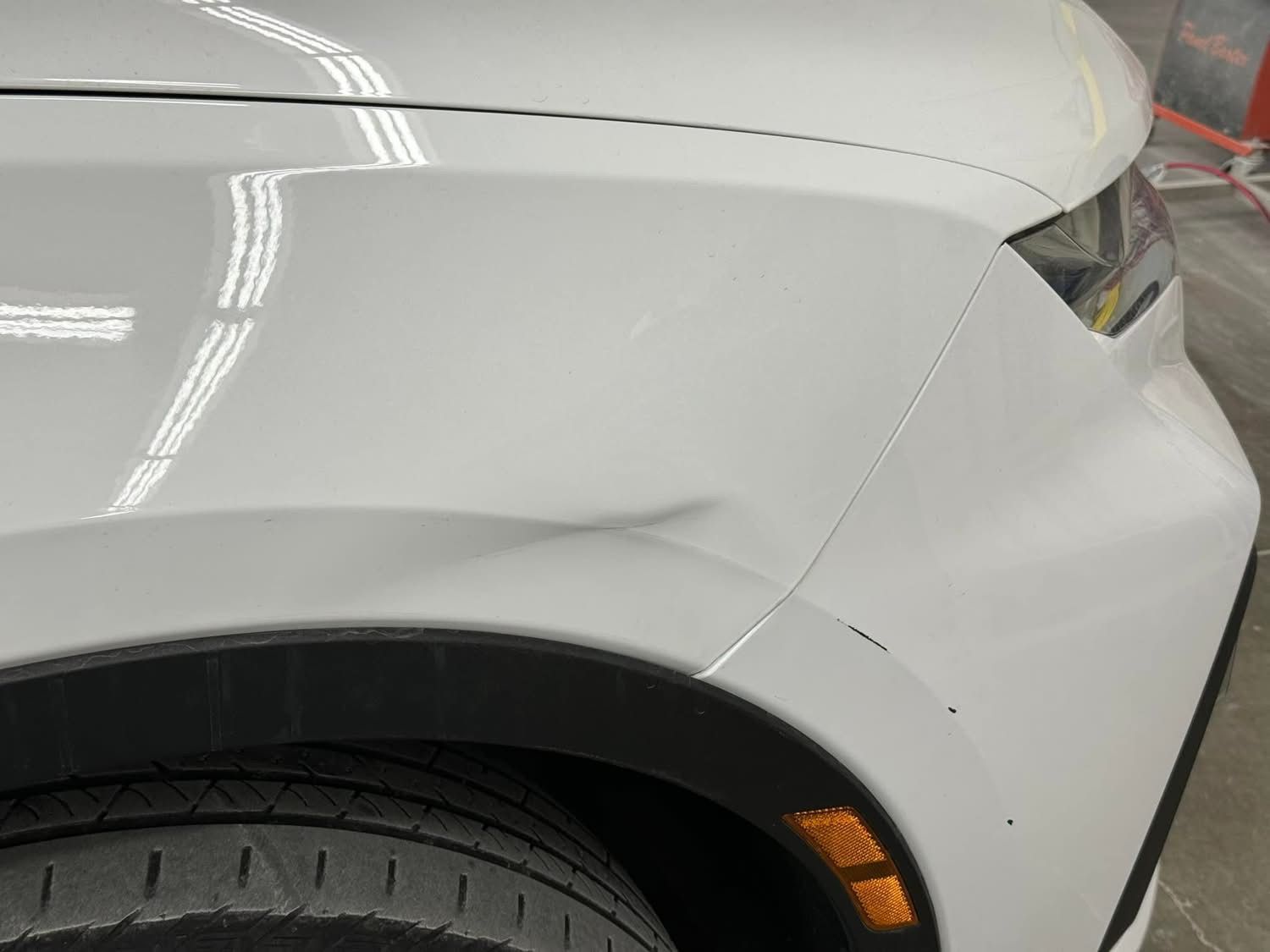 A close up of a white car with a damaged fender.
