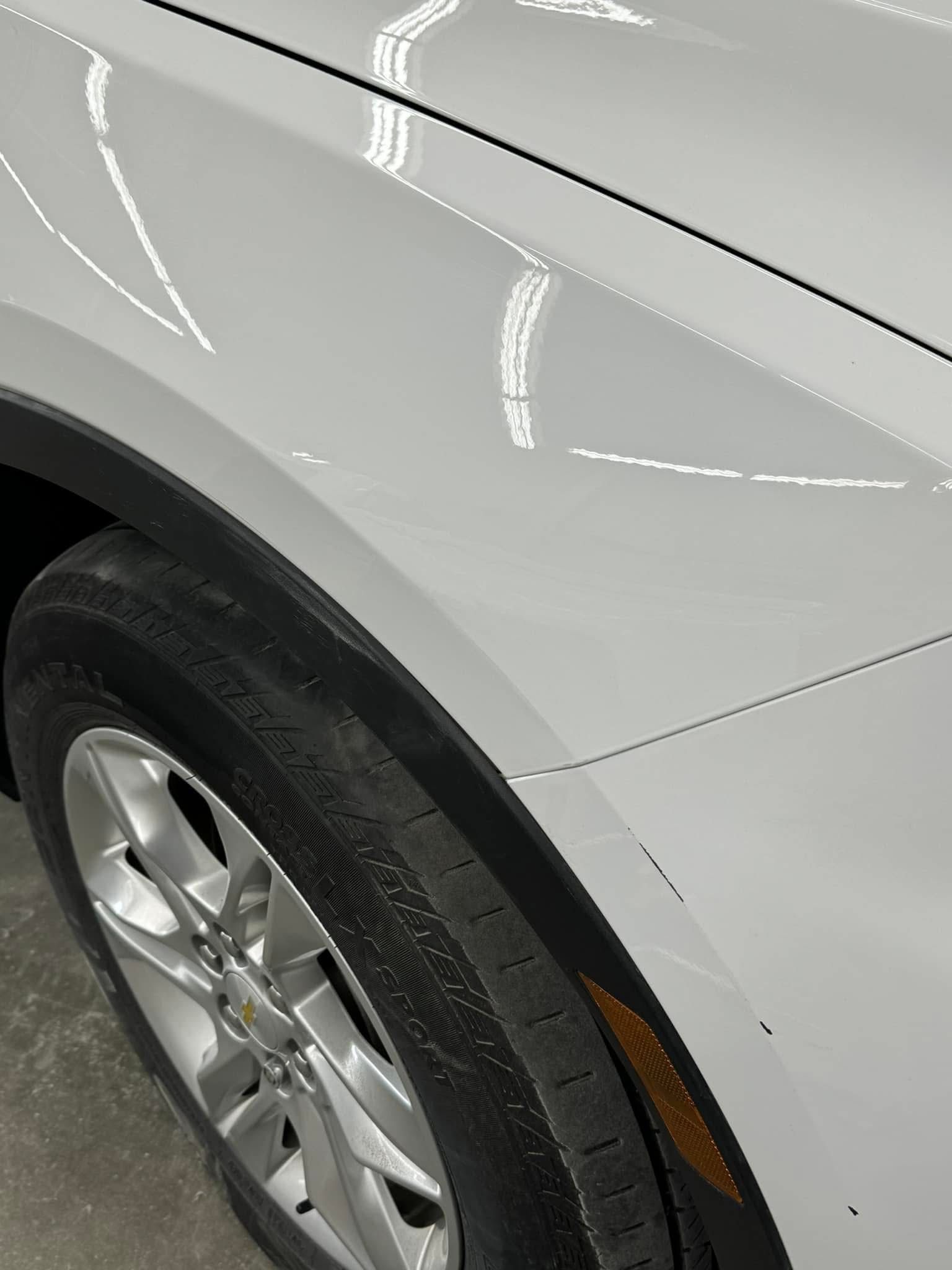 A close up of a white car 's fender and tire.
