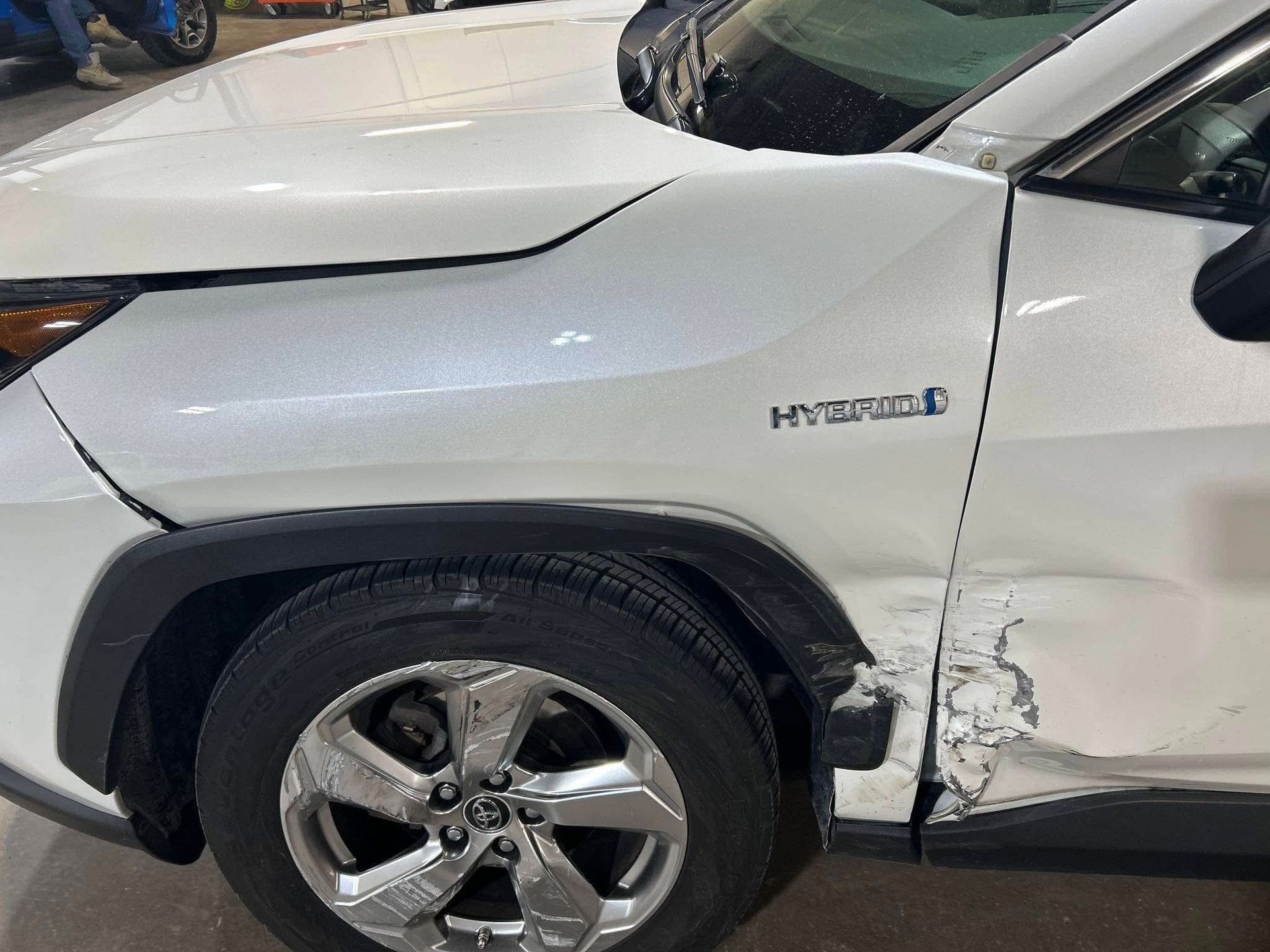 A white car with a damaged fender is parked in a garage.