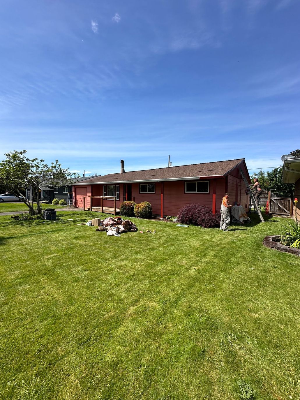 Red house with a brown roof on a green lawn under a blue sky, person standing to the right.