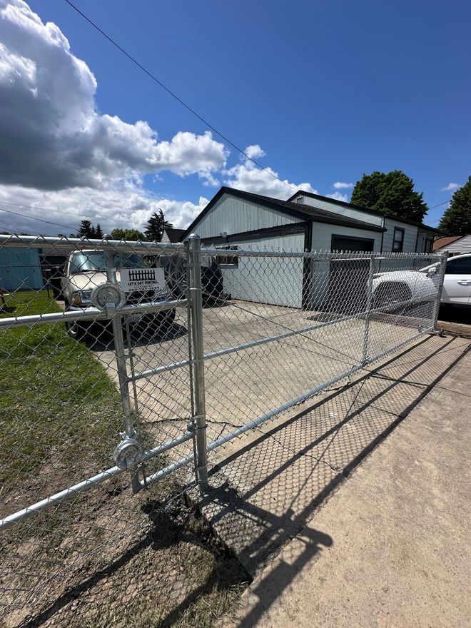 Chain link fence with gate in front of a white building on a sunny day.