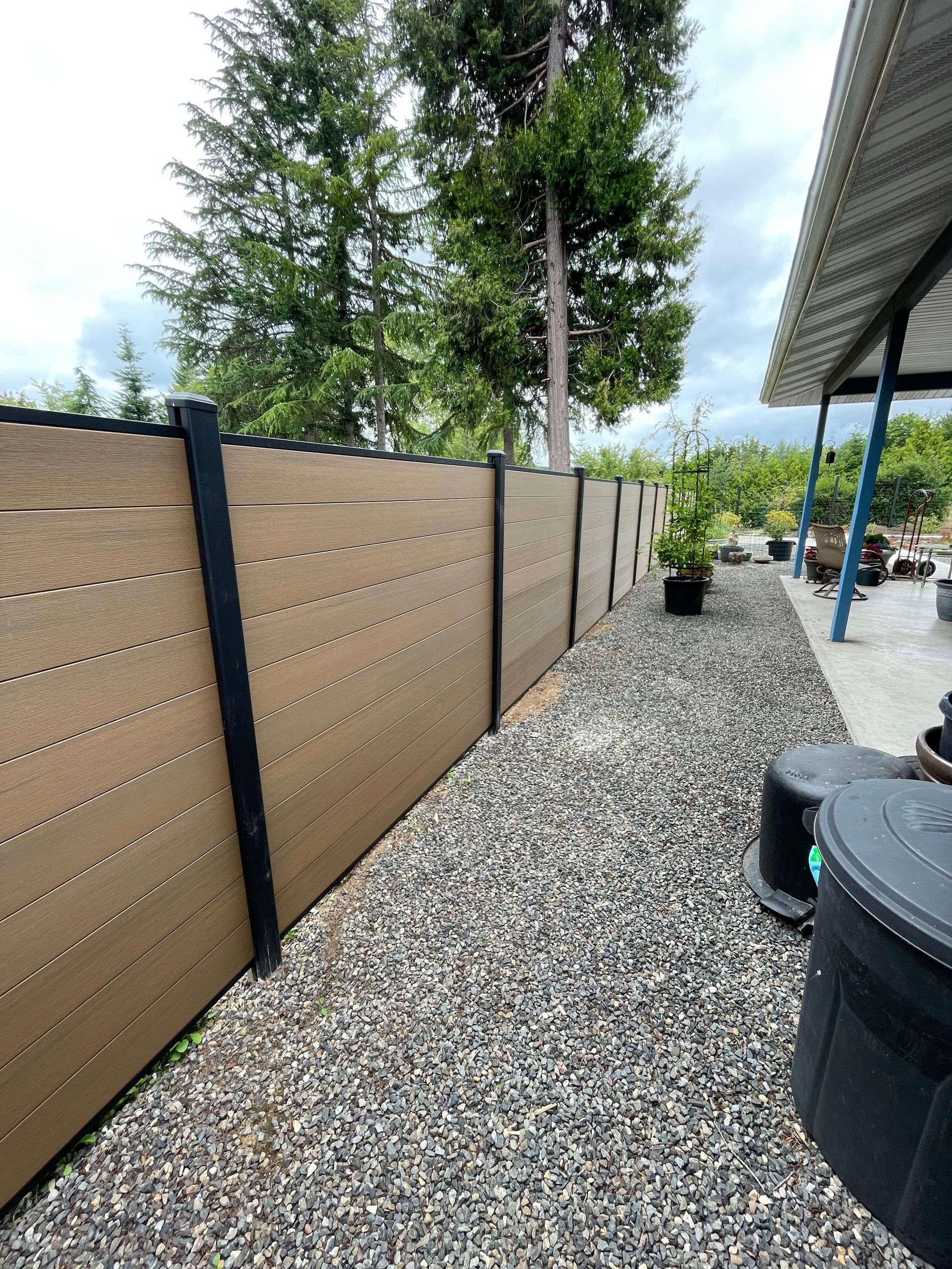 A tan horizontal slatted fence with black posts runs along a gravel path.