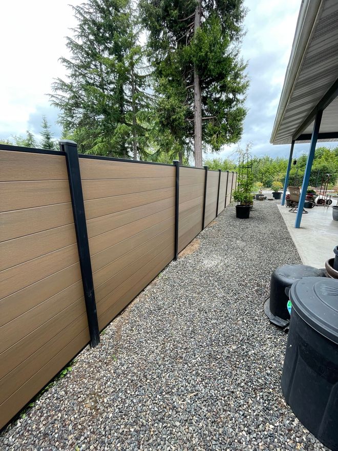 A tan horizontal slatted fence with black posts runs along a gravel path.