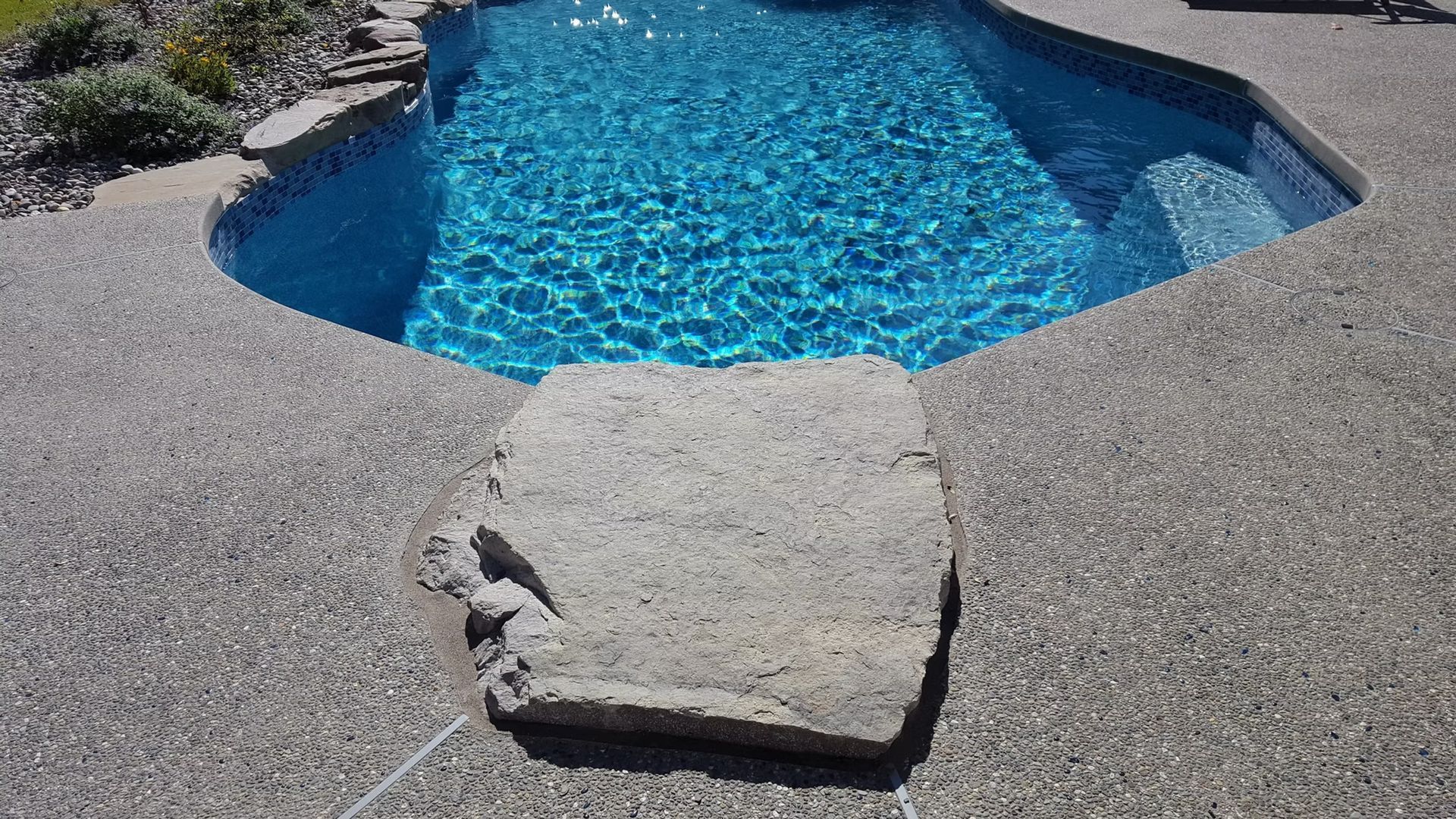 Pool with blue water and stone steps surrounded by a textured concrete deck.