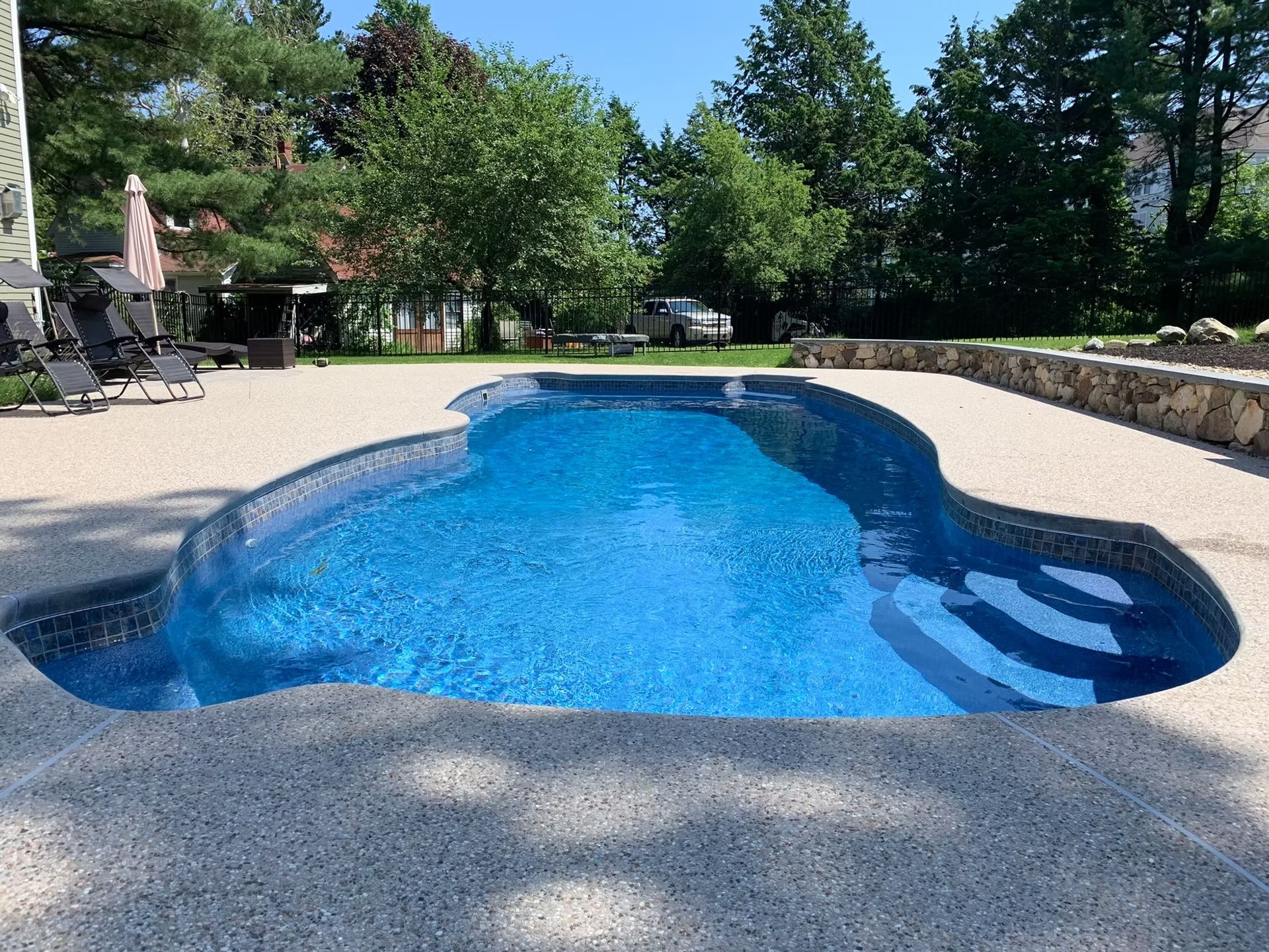 Pool with blue water and steps, surrounded by light-colored concrete patio on a sunny day.