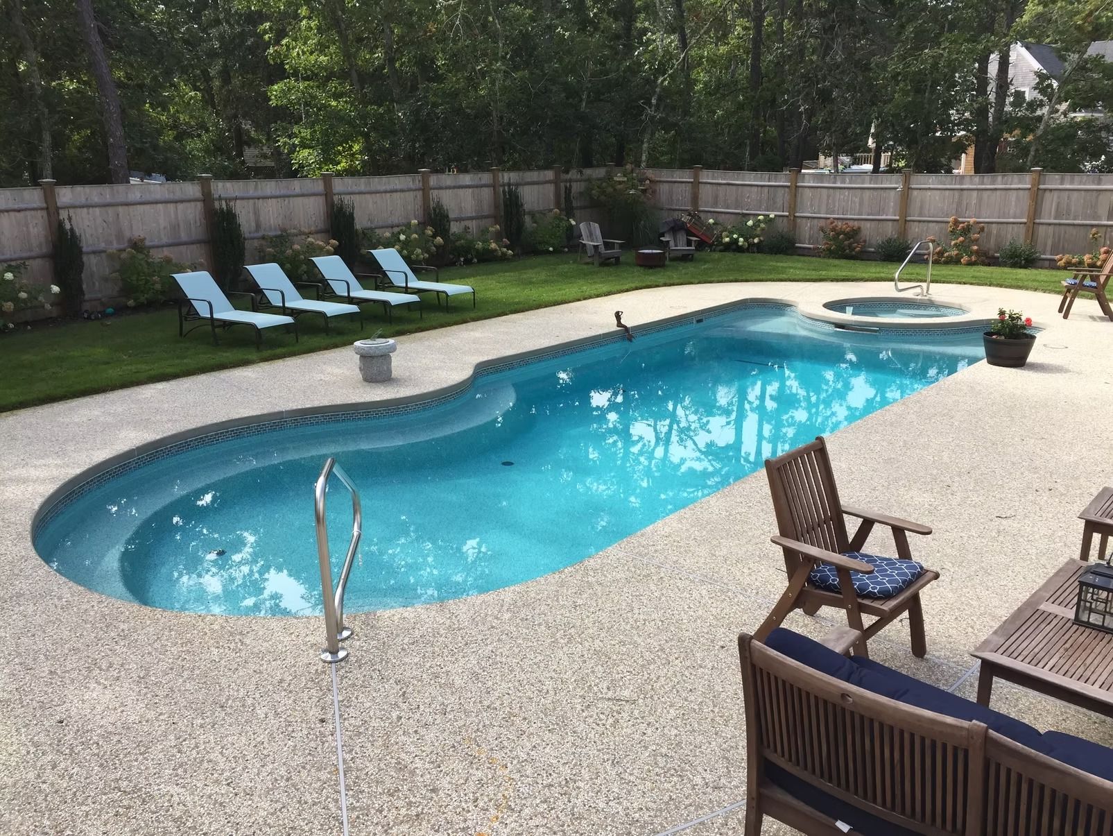 Backyard pool with lounge chairs, spa, and wooden patio furniture.