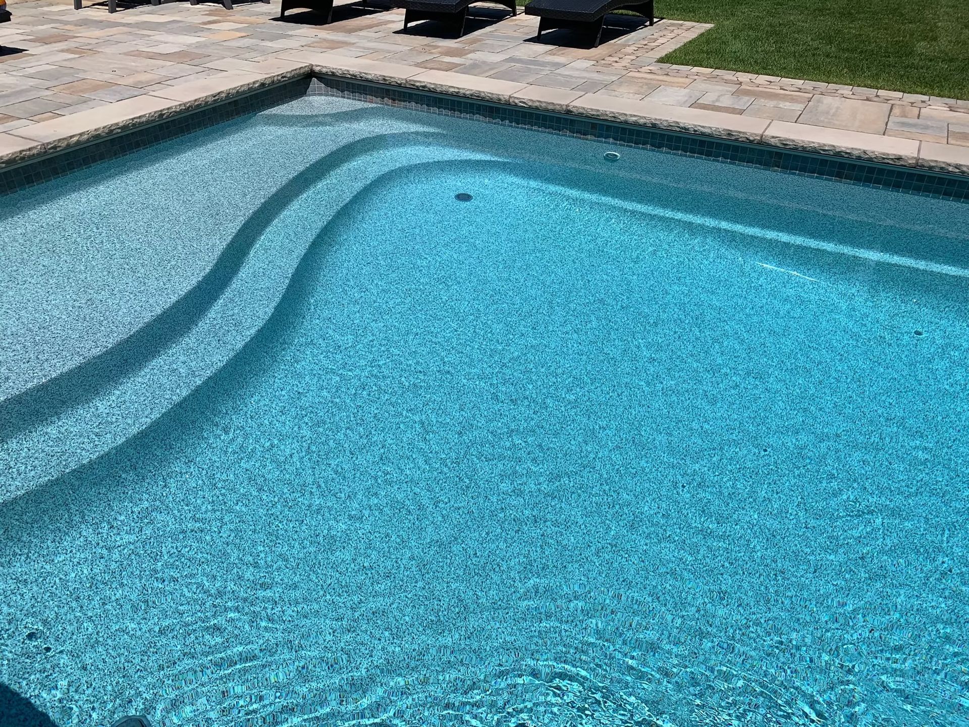 Swimming pool with built-in curved steps, filled with clear blue water, surrounded by stone patio.