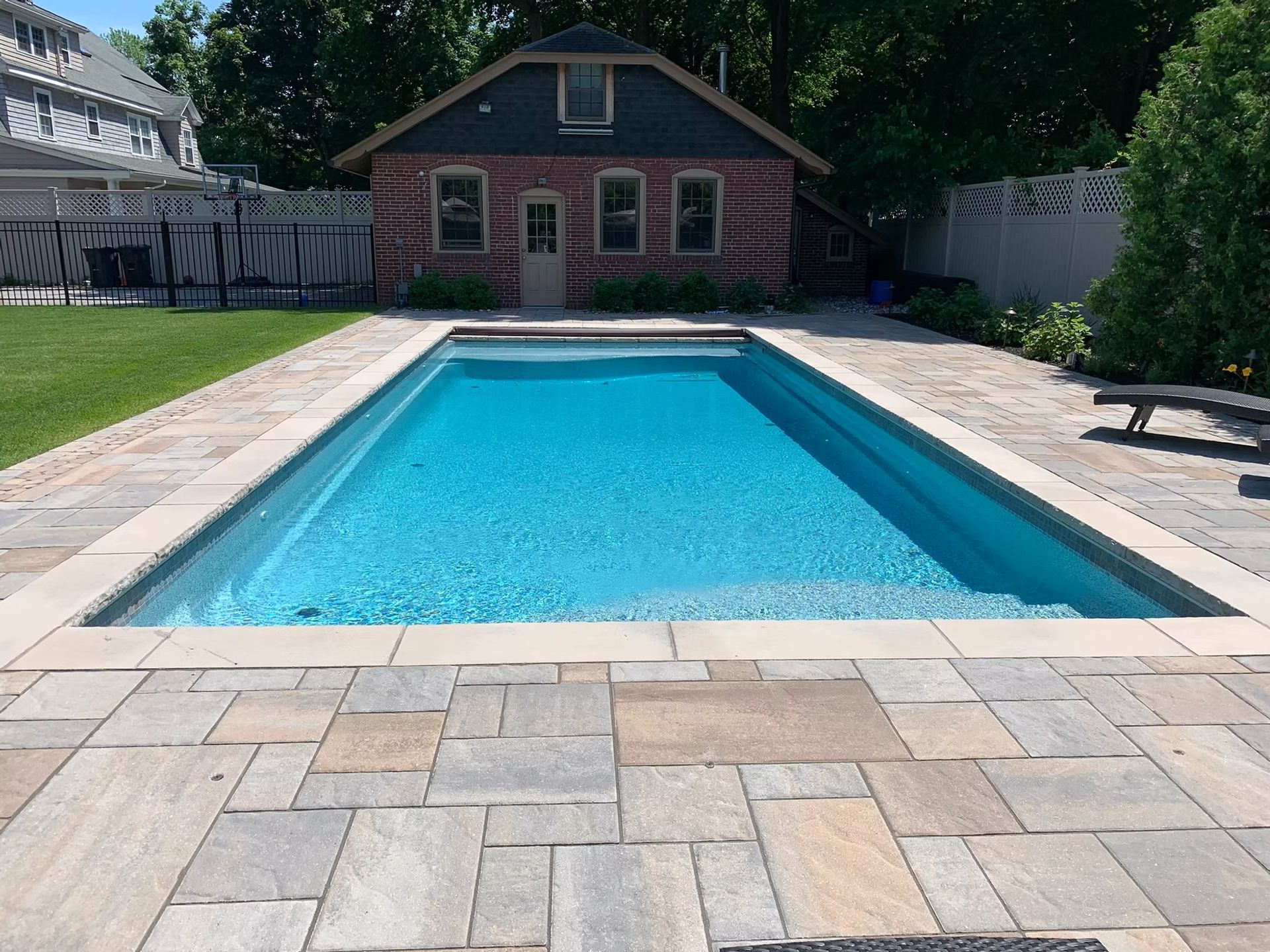 Rectangular pool with blue water, surrounded by stone patio. Red brick building in background.