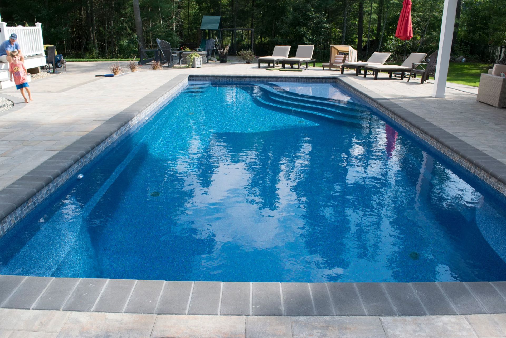 Rectangular swimming pool with blue tile interior and gray stone border.