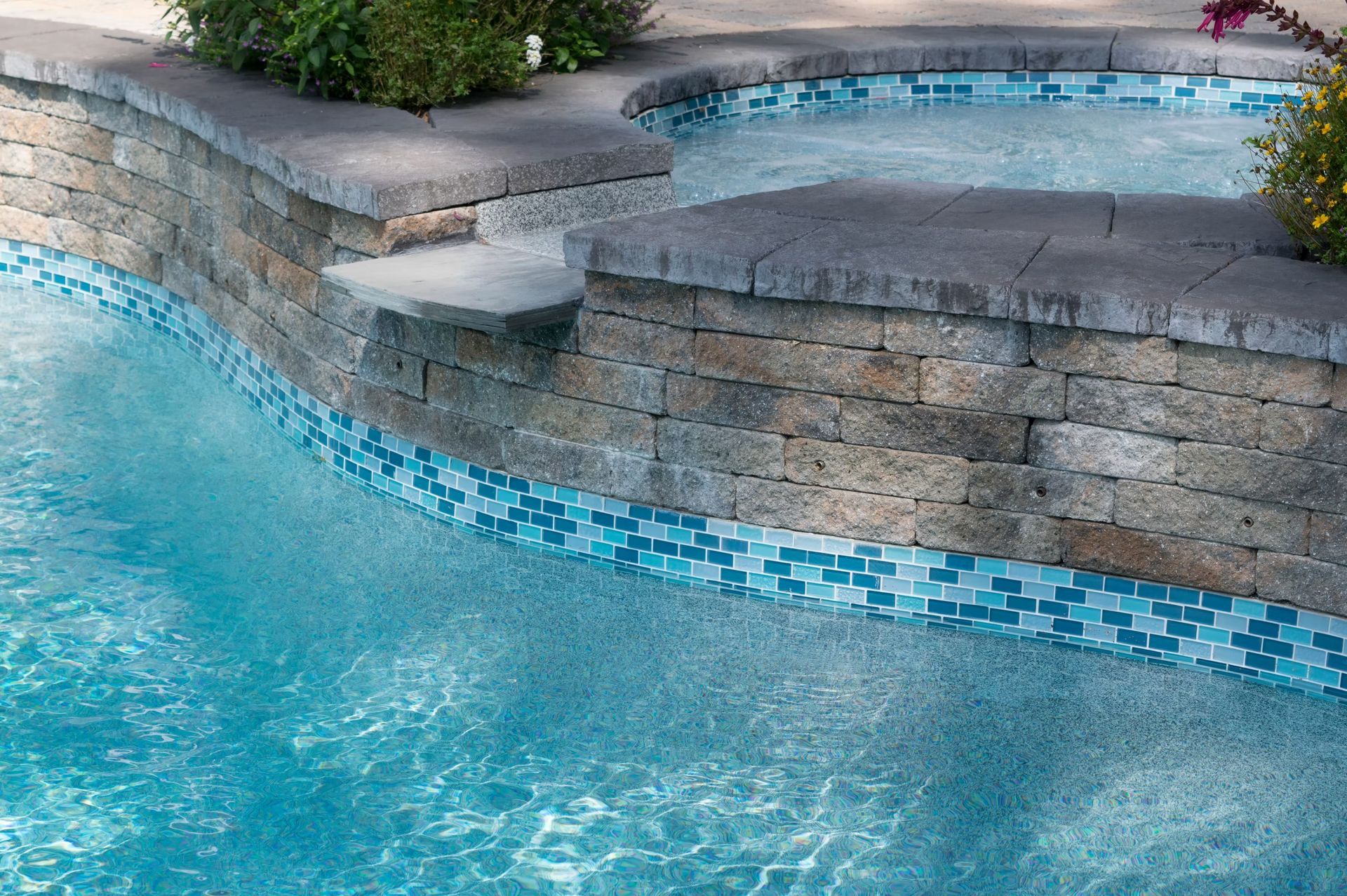 Swimming pool with brick wall, blue mosaic tile, and plants.