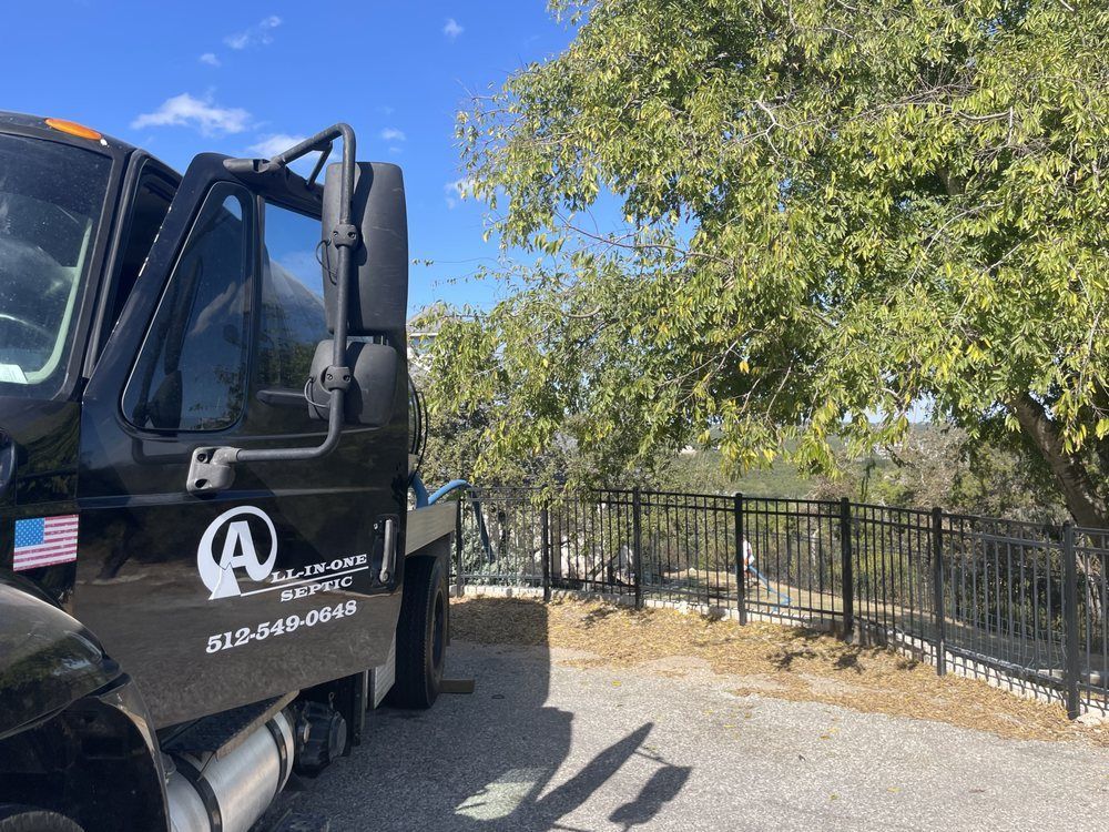 Black concrete truck parked near a black fence and a tree on a sunny day.