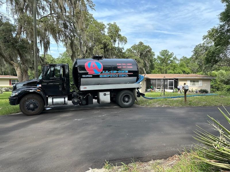 Black septic tank truck parked in front of a house, hose extended.