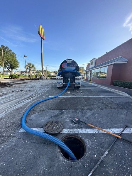 A blue hose connected to a truck is inserted into a manhole in a McDonald's parking lot.