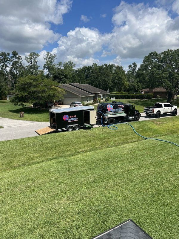 A black truck and trailer with equipment parked in front of a house on a grassy lawn.