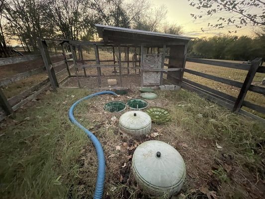Old, weathered outdoor structure with round lids and a blue hose in a grassy area.