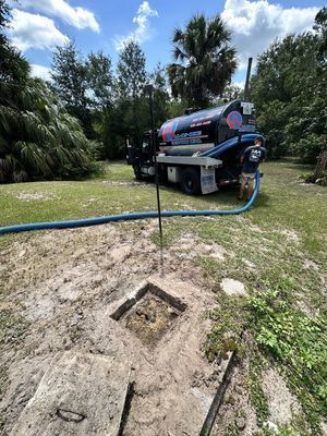 Septic tank being pumped. Truck with hose is servicing a tank in a grassy yard.