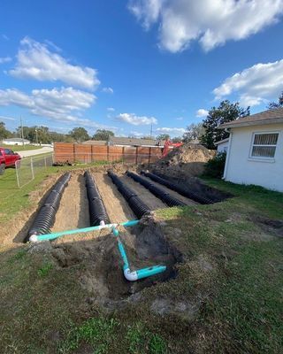 Septic system installation; trenches with black pipes, teal pipes, and dirt under a blue sky.