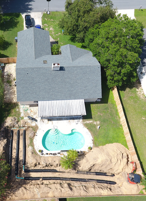 Overhead view of a house with a gray roof and a pool under construction in the backyard.