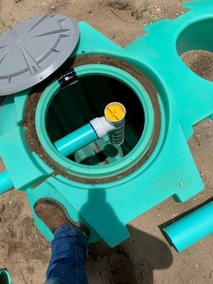 Open teal septic tank with a lid, PVC piping, and a person's foot visible.