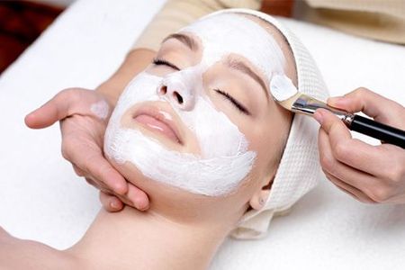 A woman is getting a white mask on her face at a spa.