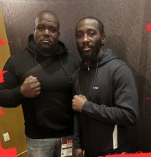 Two Black men in hoodies pose with fists clenched. One is larger, wearing jeans.
