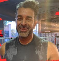 Man, sweaty, gray hair, smiling, sleeveless shirt, gym setting.