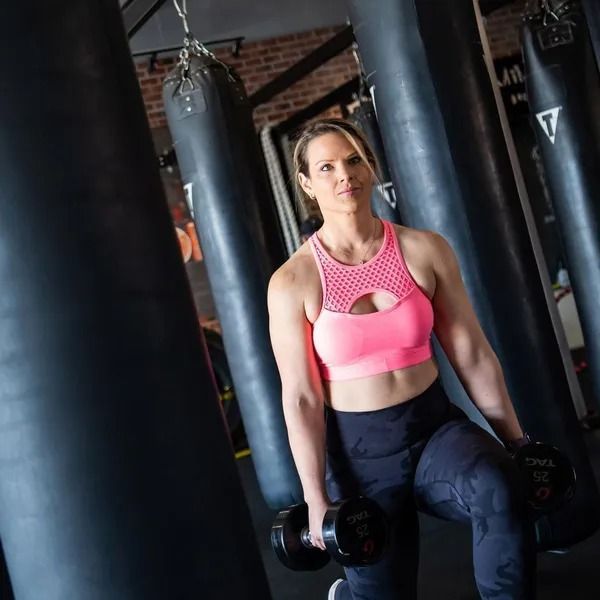 Woman in a pink sports bra and leggings working out with dumbbells in a gym.