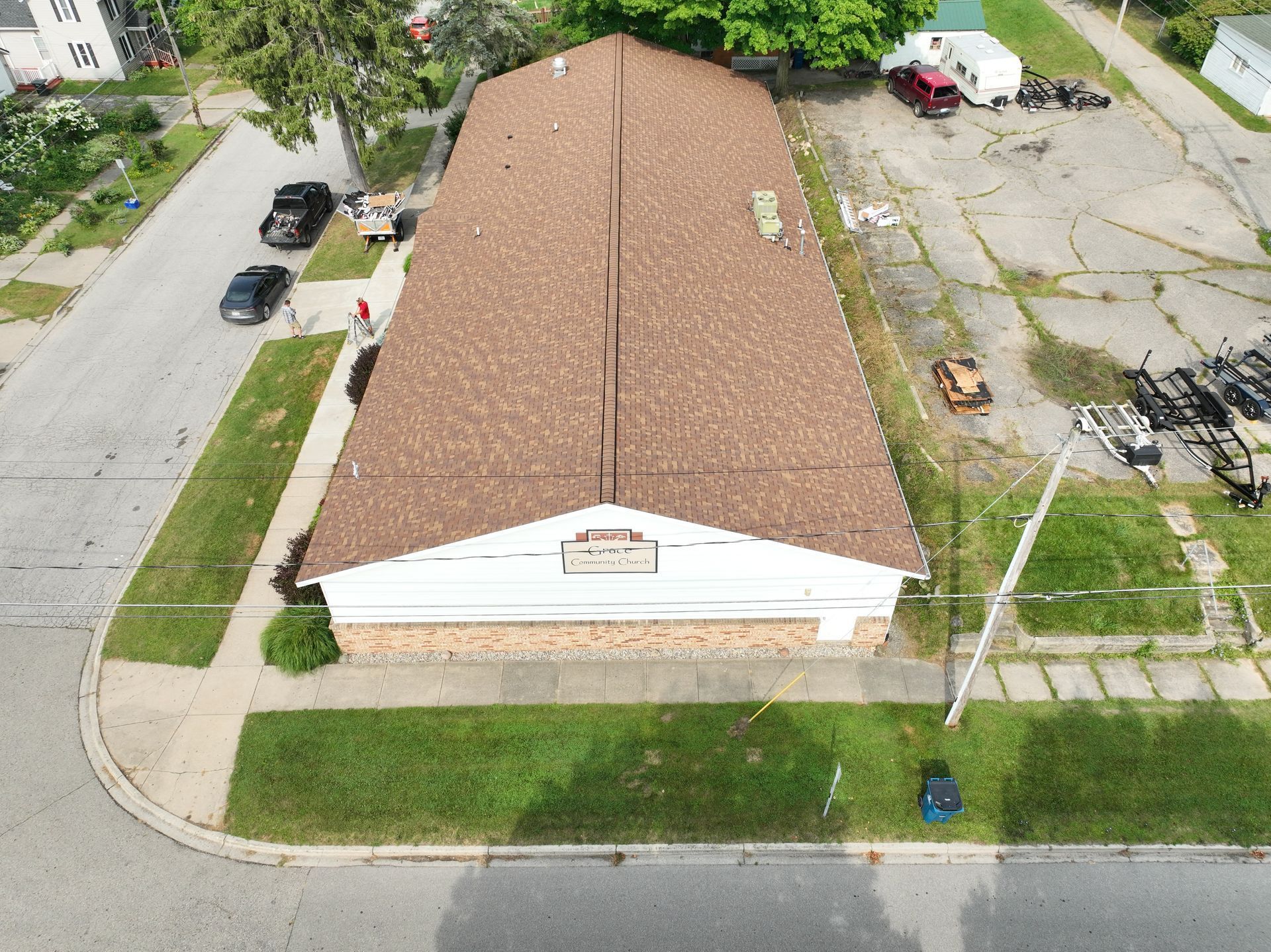 Aerial view of a tan-roofed house on a corner lot with nearby street and parking area.