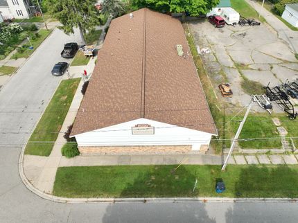 Aerial view of a tan-roofed house on a corner lot with nearby street and parking area.