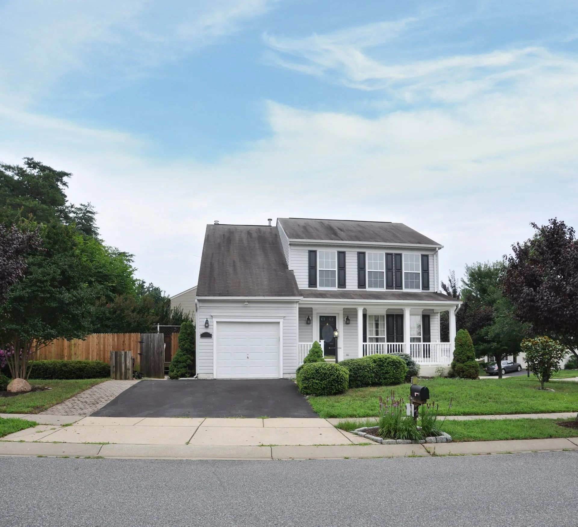 Two-story white house with attached garage, dark roof, and small front porch, set on a green lawn under a blue sky.