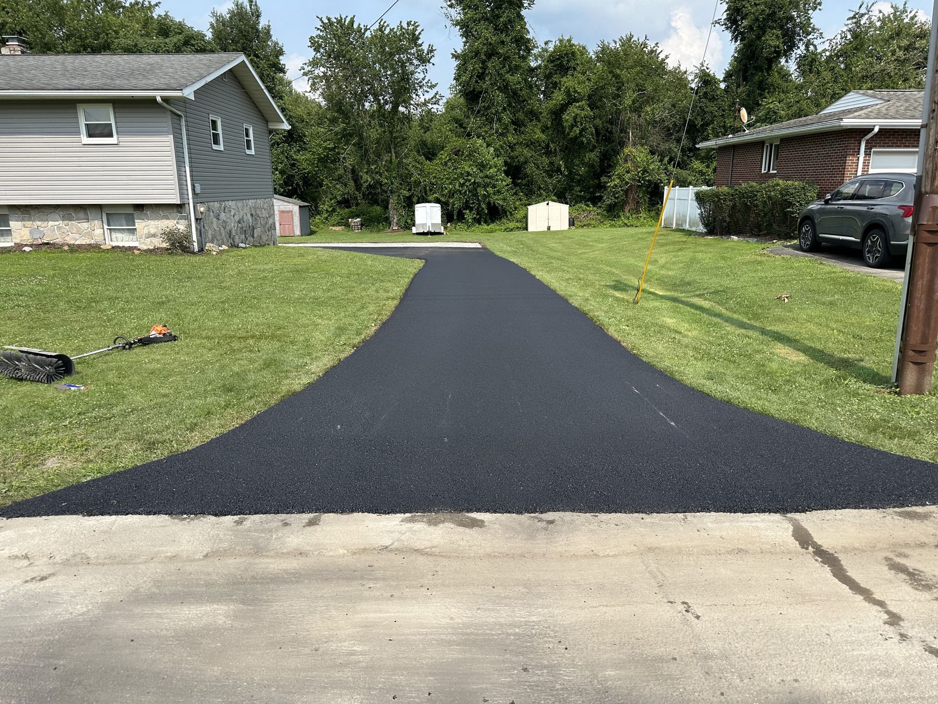 Freshly paved asphalt driveway leading from the street to a residential lawn.