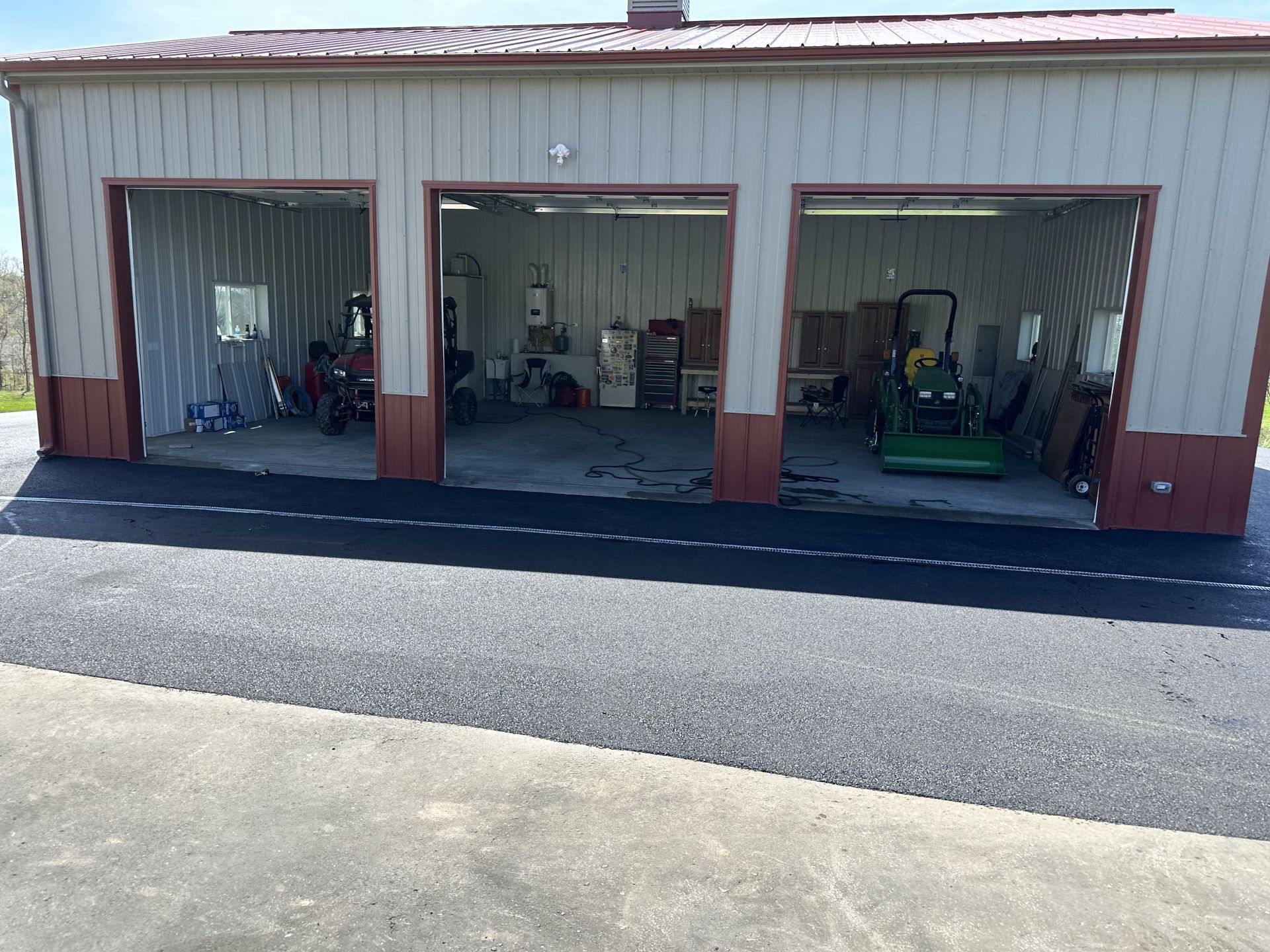 Three-bay garage with open doors, equipment inside, on freshly paved driveway.